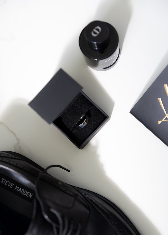 Stylish overhead view of men's accessories including shoes, a ring, and cologne on white background.